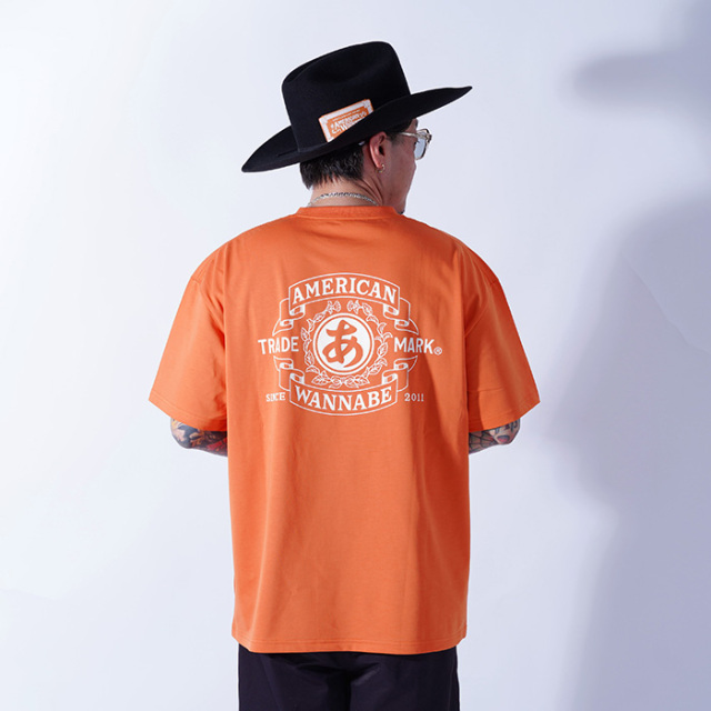 AMERICAN WANNABE/アメリカンワナビー「TRADE MARK S/S TEE / ORANGE」プリントS/S Tシャツ