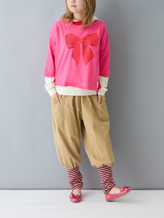 ピンクのTシャツと赤白ボーダーの裾がついたベージュのパンツを着た女性の全身