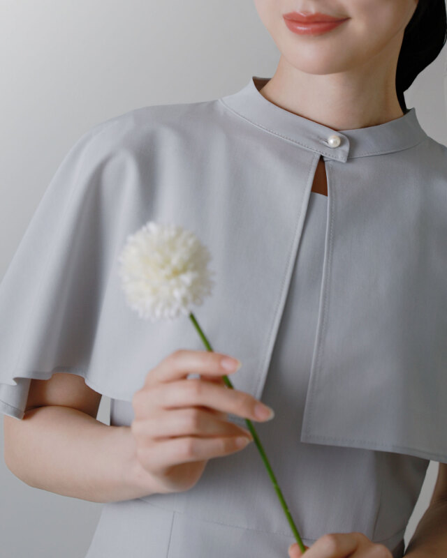 ライトグレーのワンピースを着た女性、ケープデザインが映える横向きのポーズ。大人の女性らしい洗練されたシルエット。レジーナ