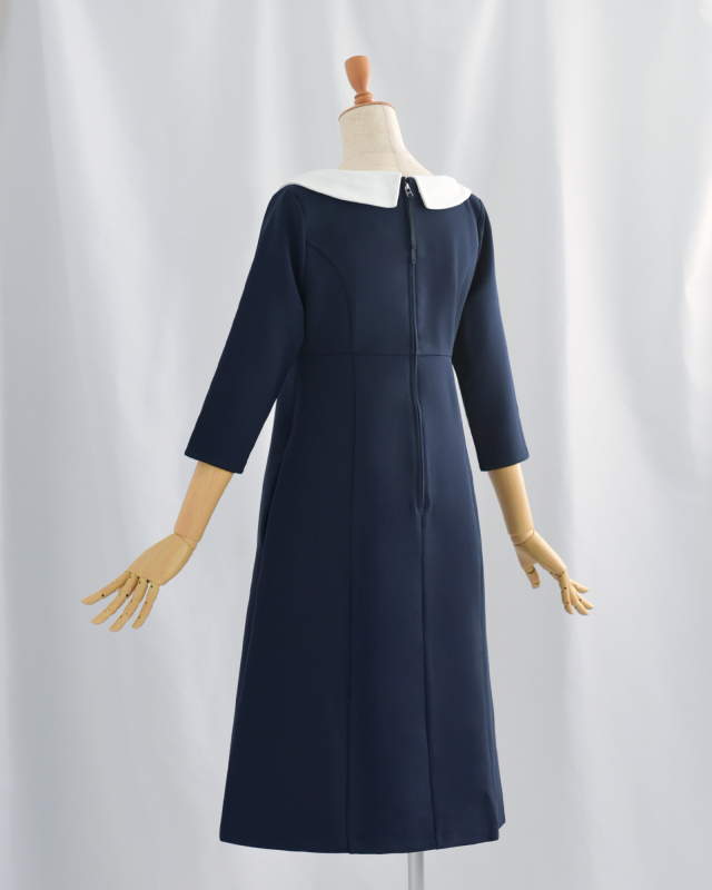 ネイビーの白襟付きワンピースを後ろ姿で見せたトルソー。上品でフォーマルなシーンにも活躍するシンプルデザイン。