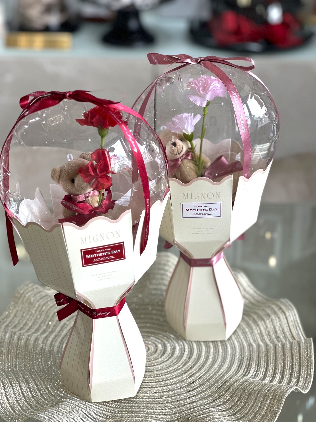 透明なバルーンの中に一輪のカーネーションを抱えたクマのぬいぐるみが入った自立型ブーケ。レッドとピンクの2色。母の日ギフト。