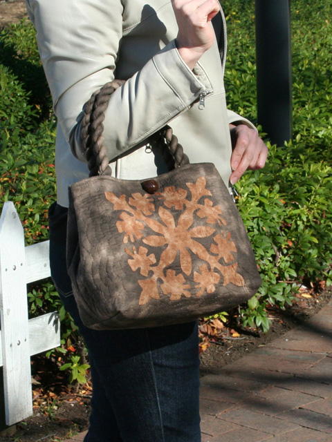 こげ茶地に茶色のハイビスカスが幾何学模様にデザインされたハワイアンキルトセカンドバッグ。肘にかけた画像