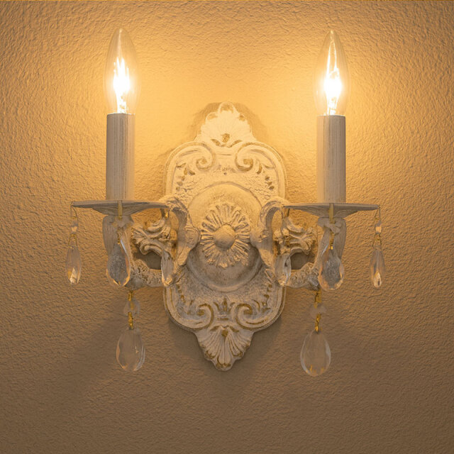 白い装飾ブラケット照明が壁に取り付けられ、柔らかな光を放つ設置例