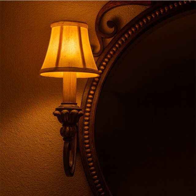 クラシックデザインの照明付きミラーのランプが点灯し、暖色の柔らかい光がシェード越しに広がるアンティーク調のクローズアップ写真。