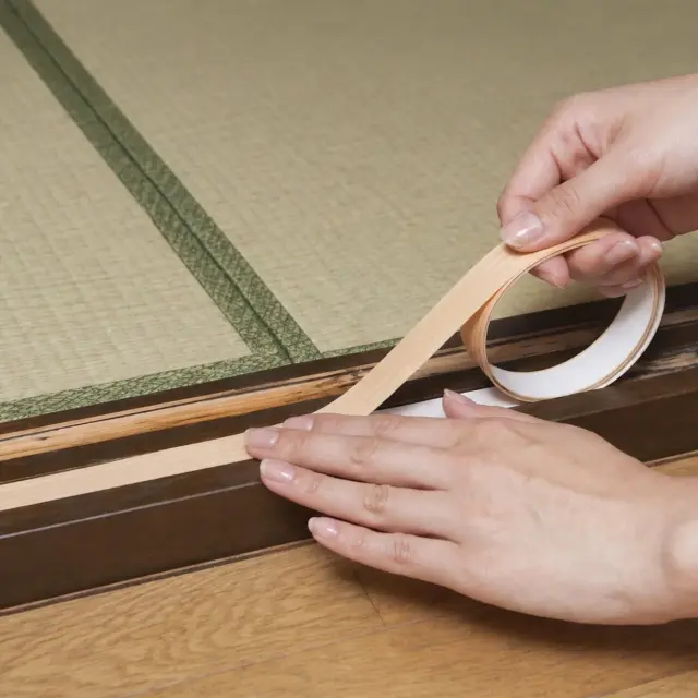 敷居すべりの貼り方 女性の手で敷居にテープを貼る施工イメージ